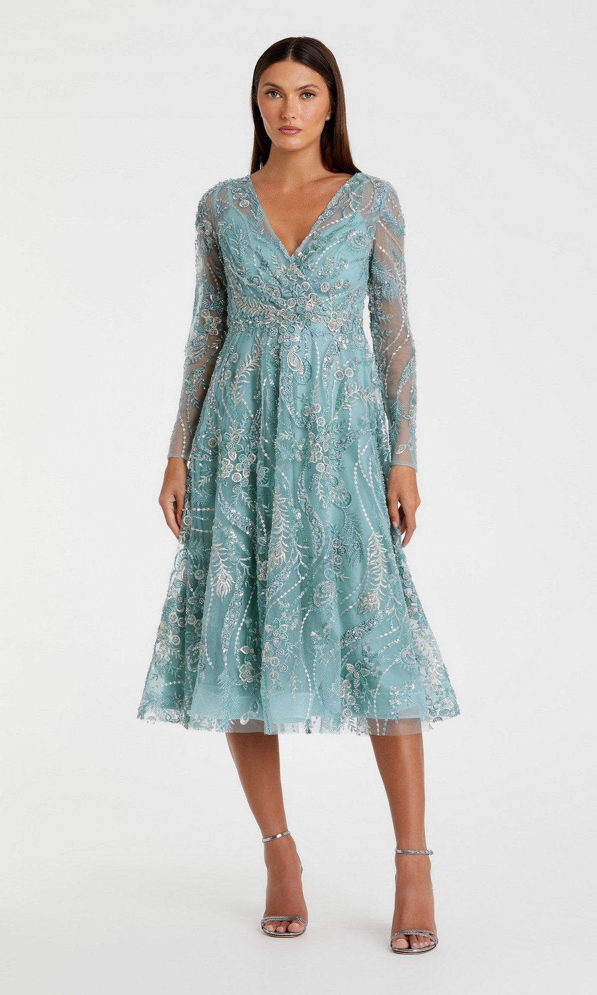 A woman wearing the Mac Duggal 68915 Midi Party Dress in seafoam, featuring long sleeves, a V-neckline, fit-and-flare silhouette with silver embroidery, stands in strappy silver heels against a plain white background.
